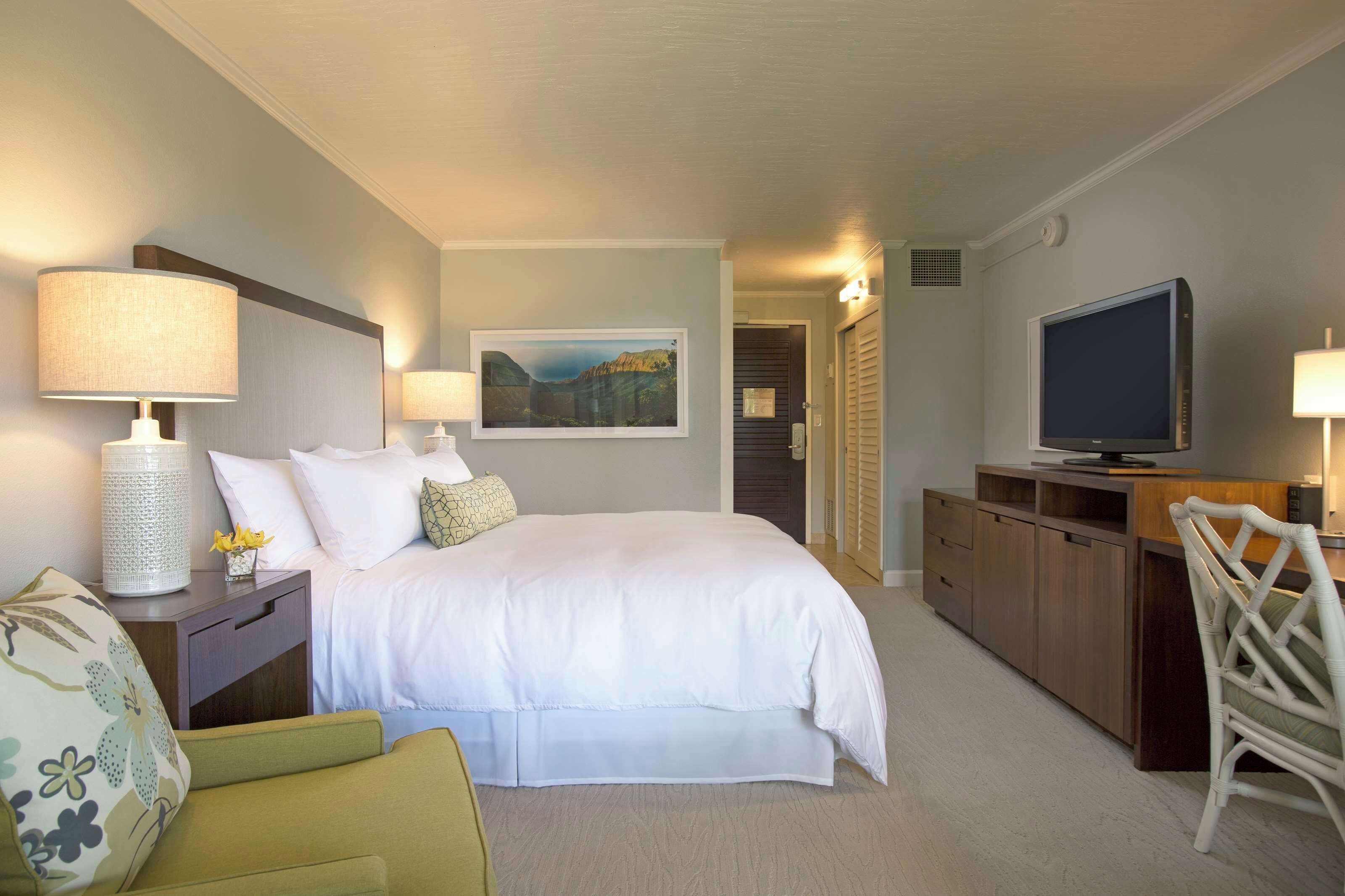 Una habitación de hotel con cama, lámparas de noche, televisión, escritorio y una silla.