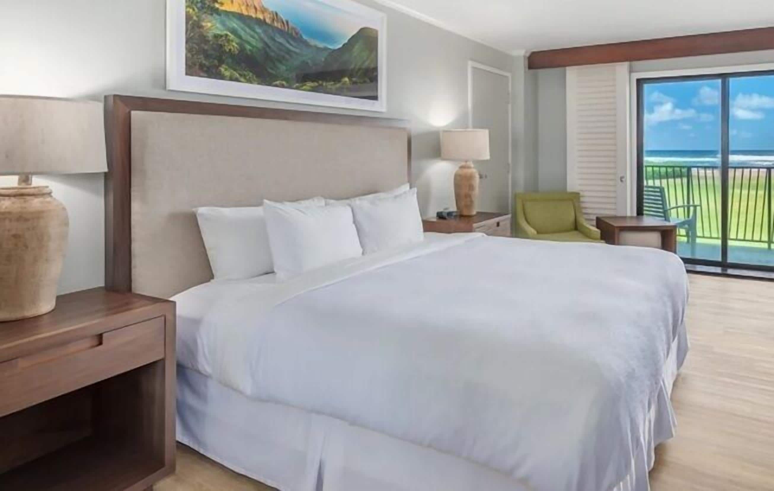 A hotel room with a large bed, a nightstand, a chair, a table, and a balcony with a view.