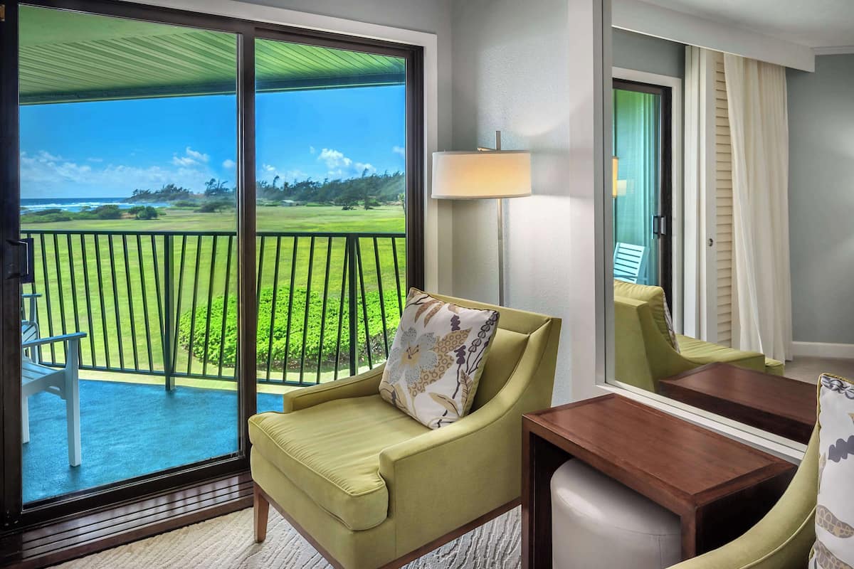 A room with a sliding glass door leading to a balcony with a view of a green landscape and ocean.