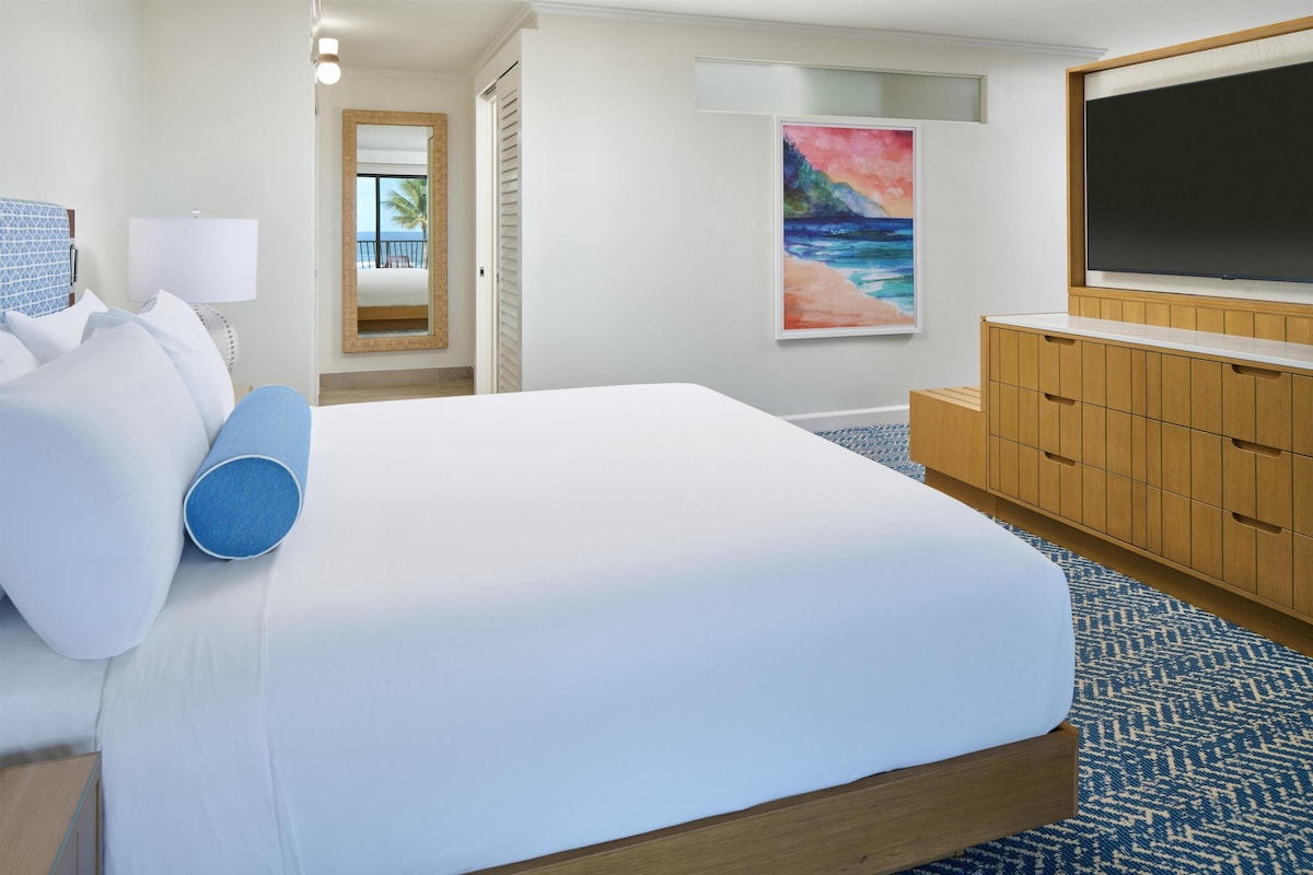 Una habitación de hotel con una cama grande, un televisor, un armario de madera y un cuadro con una playa.