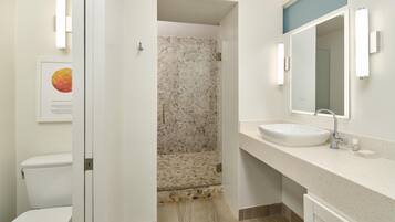 A bathroom with a white sink, a mirror, a framed picture on the wall, and a shower with a stone wall.
