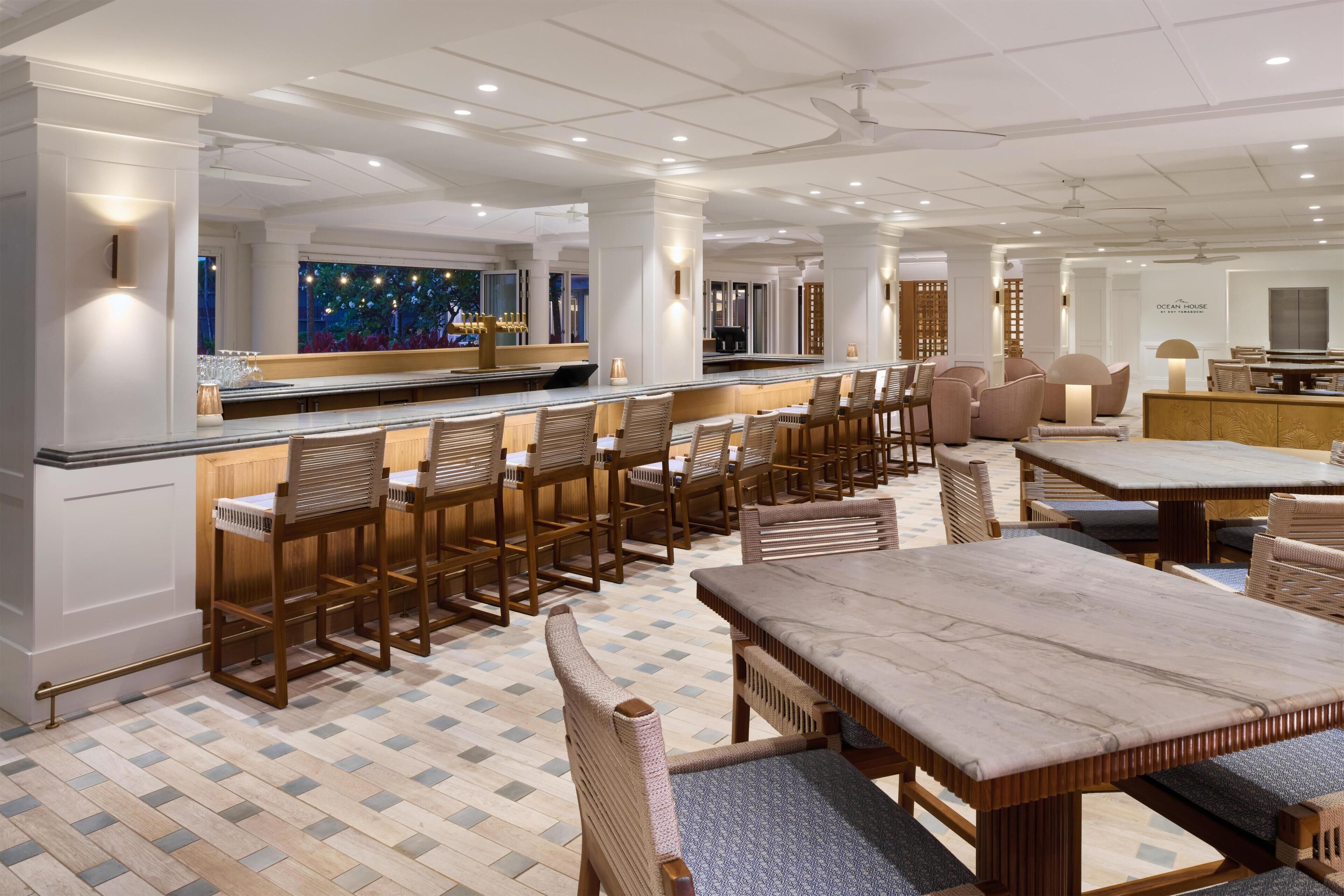 A modern hotel lobby with a bar area, seating arrangements, and a view of the night sky.