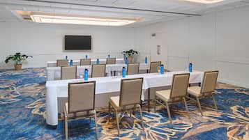 A conference room with a long table, chairs, a flat-screen TV, and a patterned carpet.