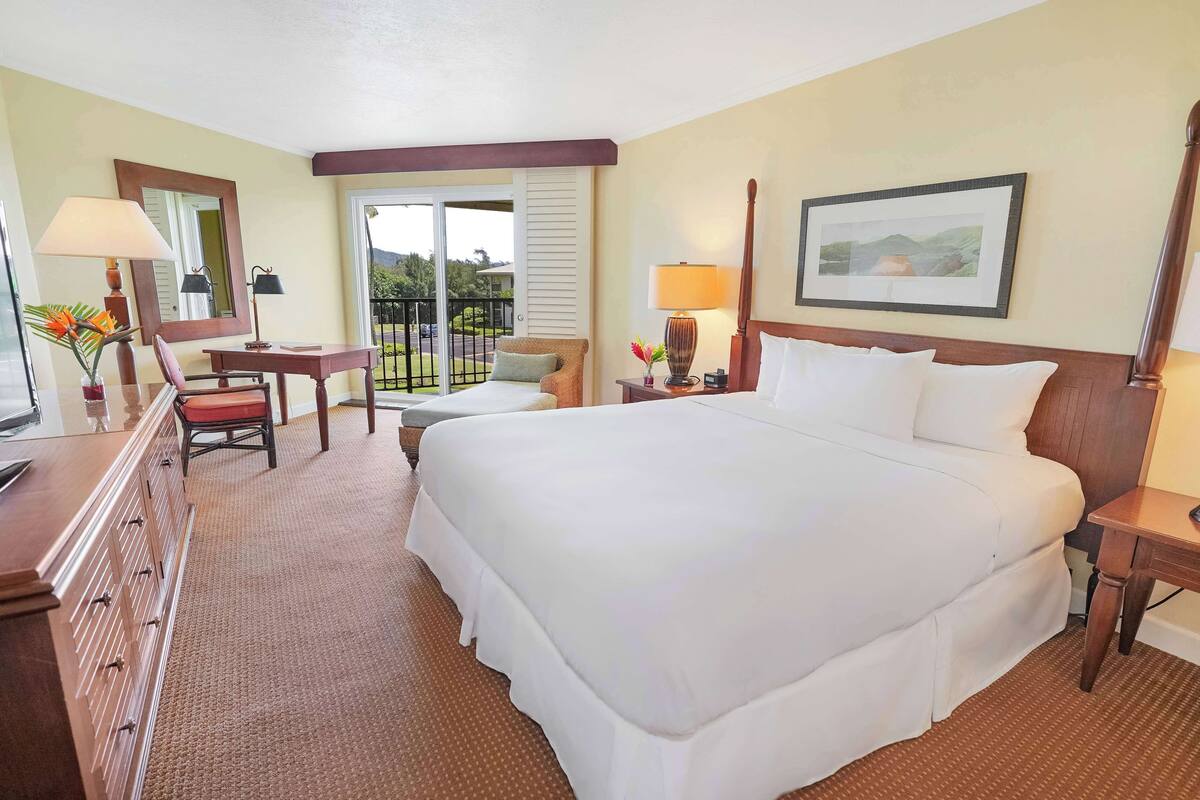 A hotel room with a large bed, a desk, a chair, a lamp, and a picture on the wall.