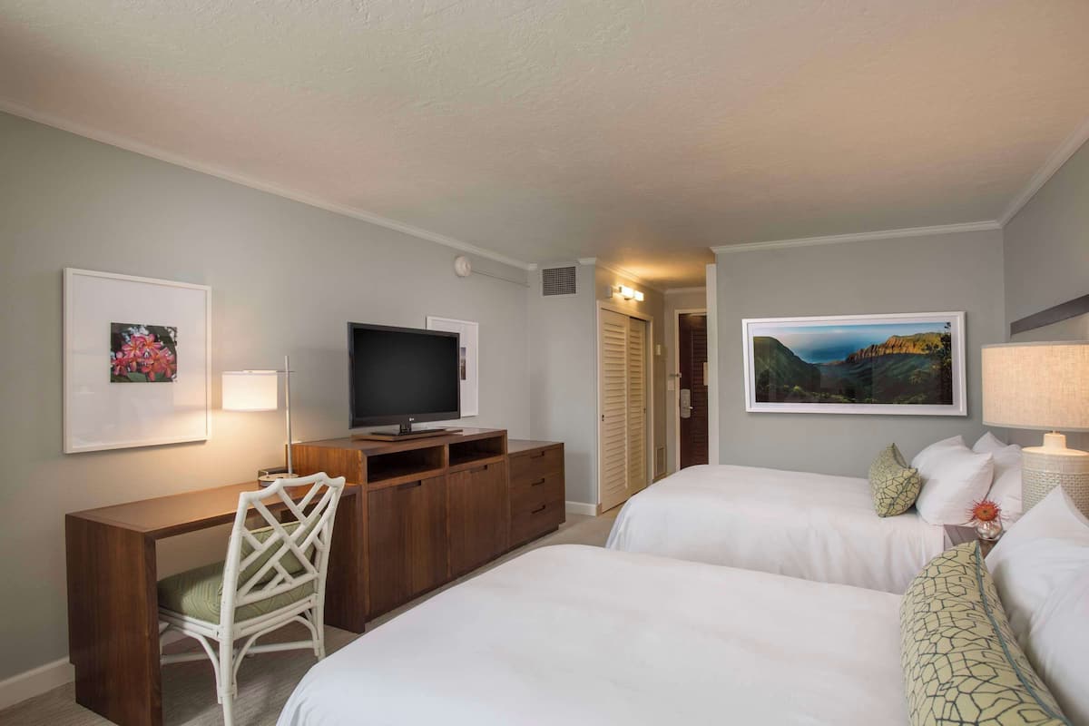 A hotel room with two beds, a desk with a TV, a chair, and artwork on the walls.