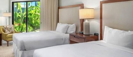 A hotel room with two beds, a nightstand with a lamp, a chair, and a view of greenery outside.