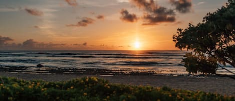 Un coucher de soleil sur l’océan, avec une plage au premier plan.