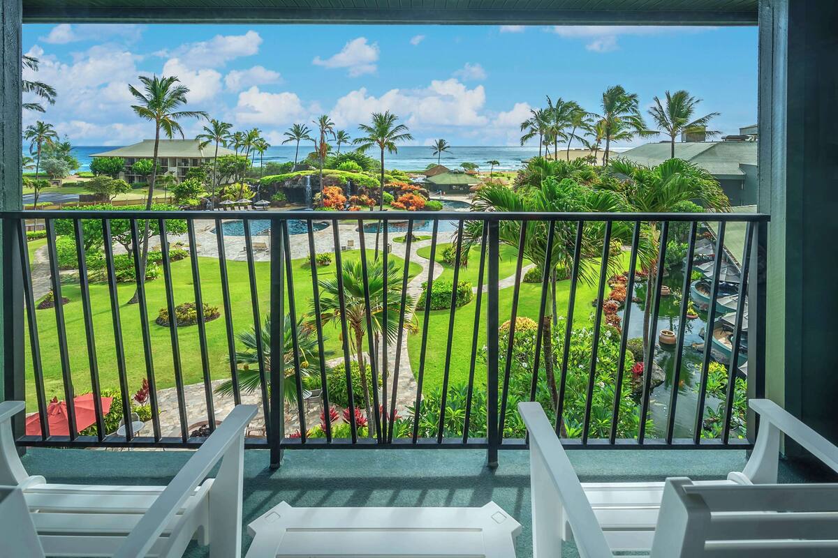 A balcony with a view of a landscaped garden, a pool, and the ocean.