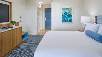 A hotel room with a bed, a TV, a painting, a lamp, and a wooden dresser.
