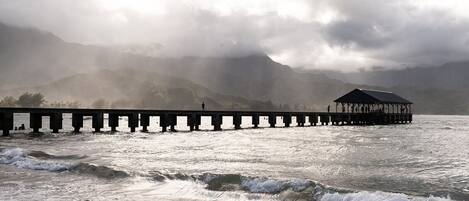 A pier extending into a body of water with waves crashing onto the shore.