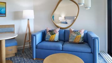 A modern hotel room with a blue sofa, a round wooden table, a mirror, and a patterned floor.