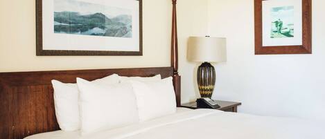 A hotel room with a large bed, a wooden headboard, a nightstand with a lamp, and two framed pictures on the wall.
