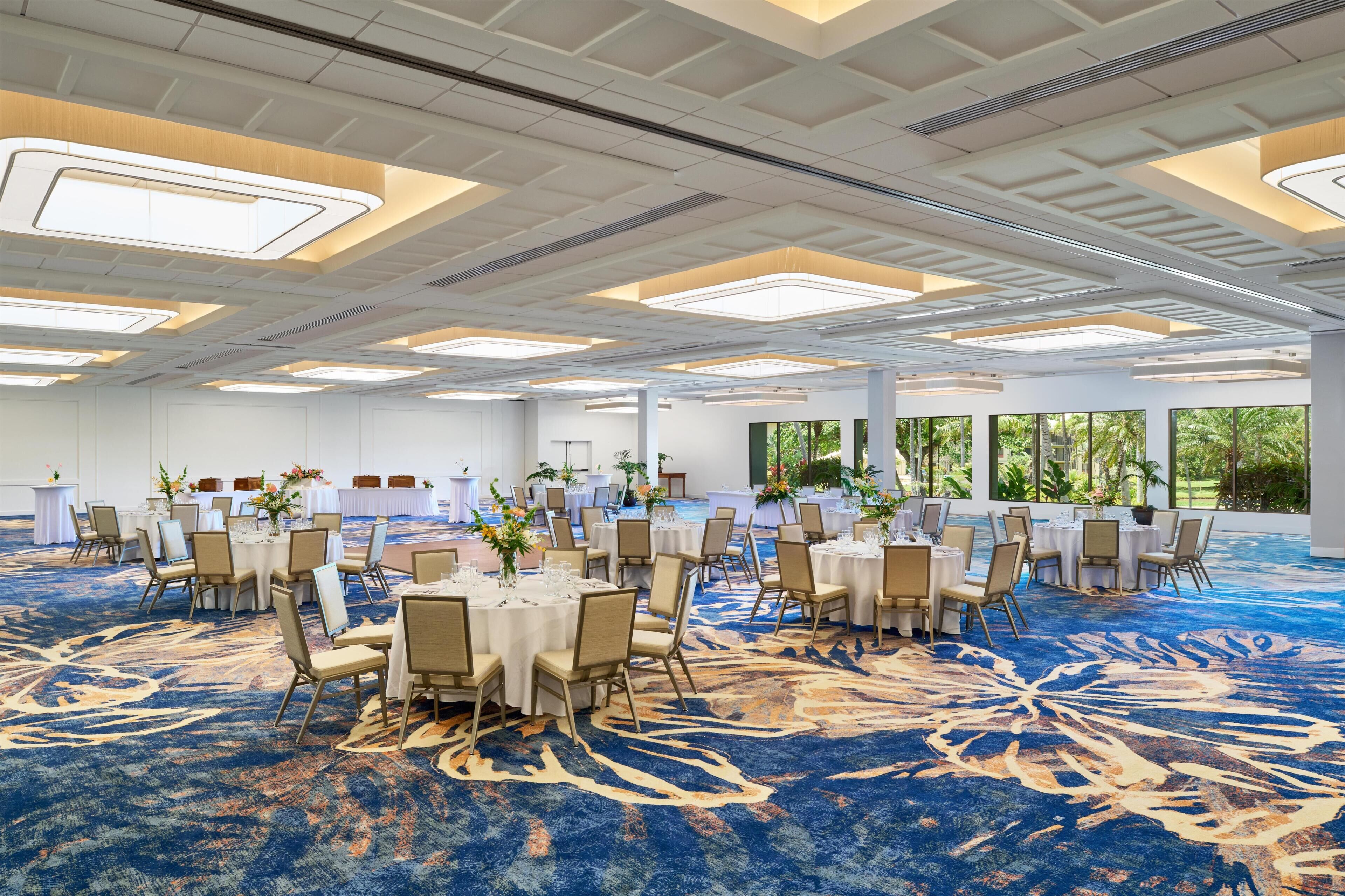 A large conference room with round tables, chairs, and a blue carpet.