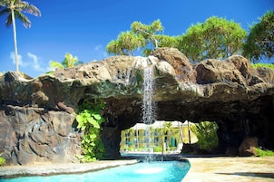 Uma piscina com cachoeira, formação rochosa e um edifício ao fundo.