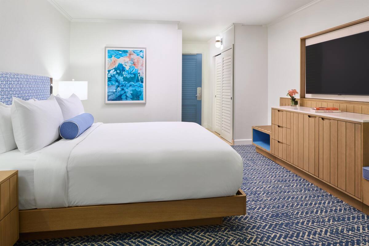 A hotel room with a bed, a TV, a painting, and a wardrobe.