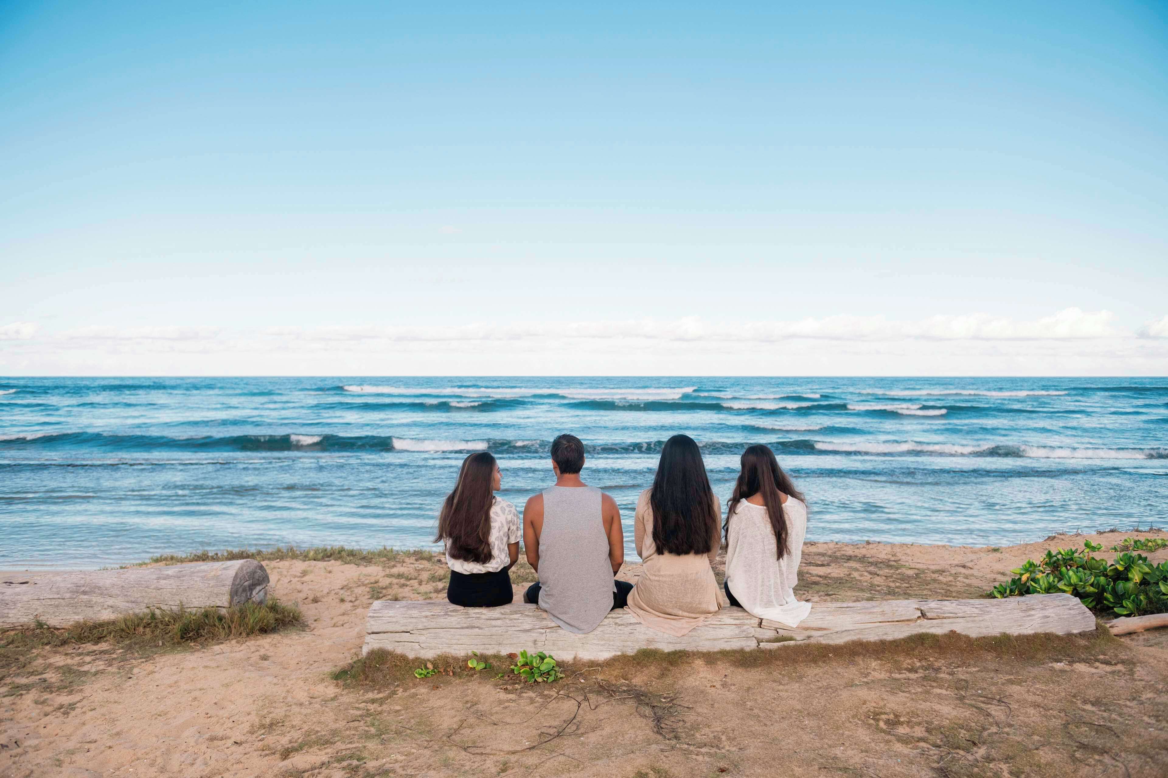 Four people sitting on a wooden bench by the ocean.