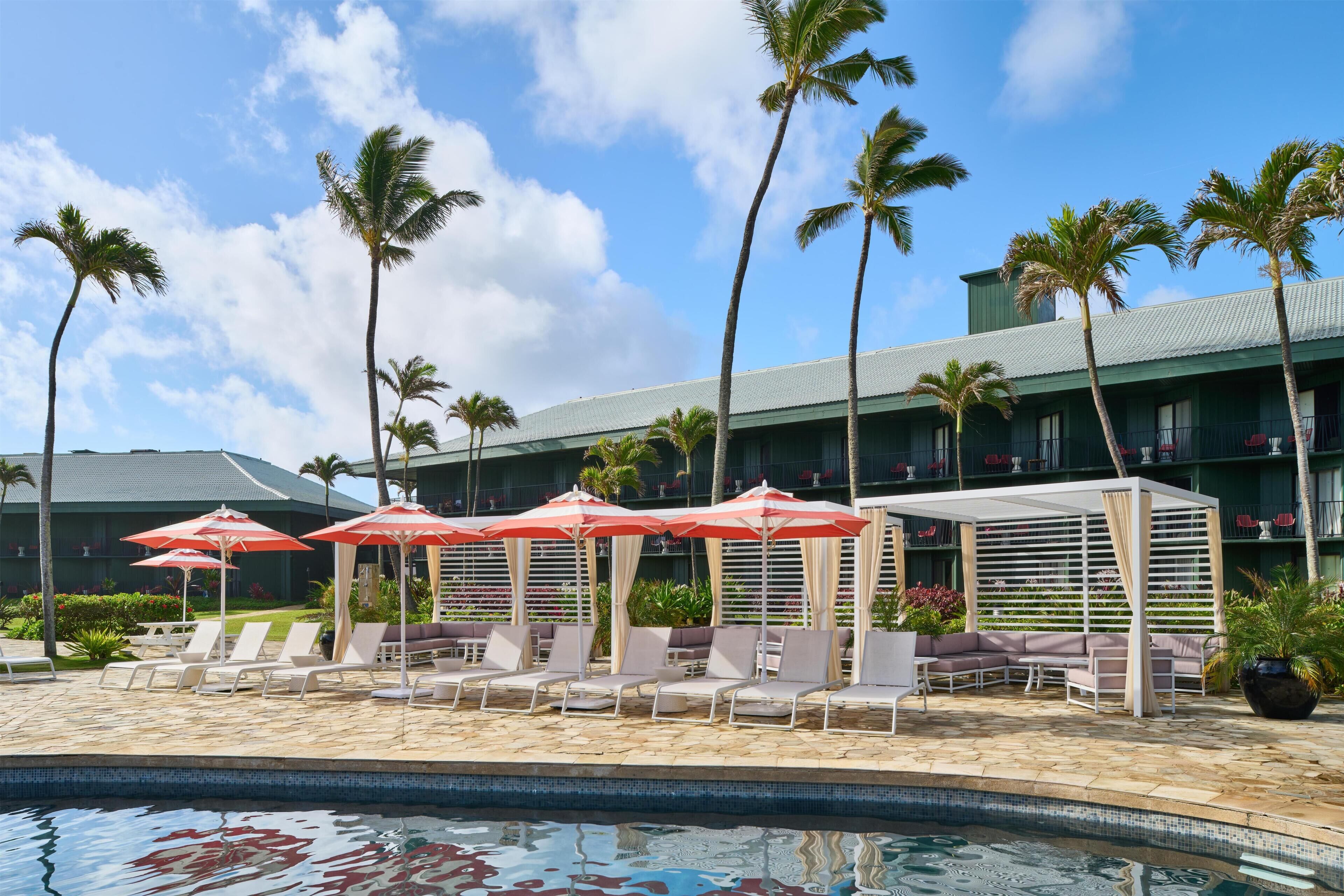 A poolside area with lounge chairs, umbrellas, and palm trees.