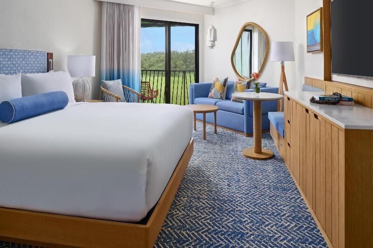 Une chambre d’hôtel avec un grand lit, un canapé, une petite table, un miroir et une vue sur l’extérieur.