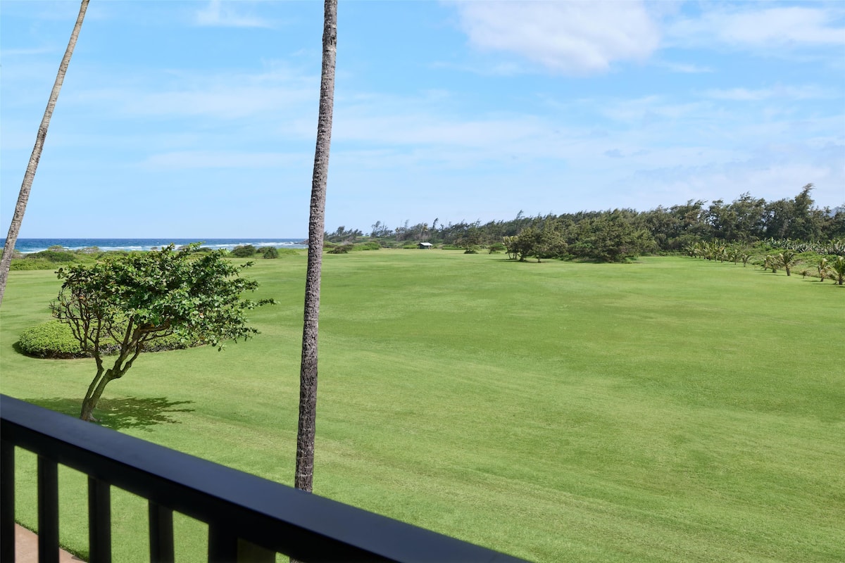 Un campo de golf con vista despejada al océano, un césped bien cuidado y algunos árboles.