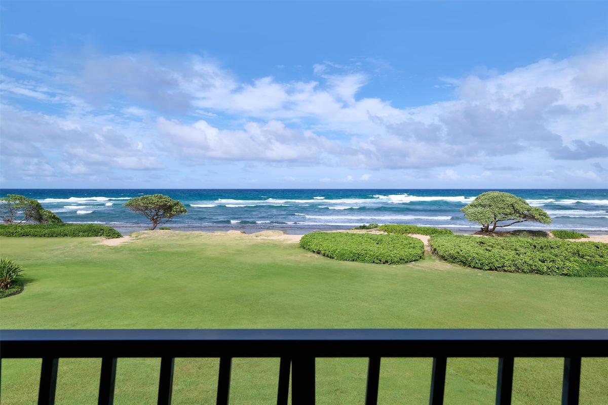 A view of the ocean with waves, a grassy area, and two trees.