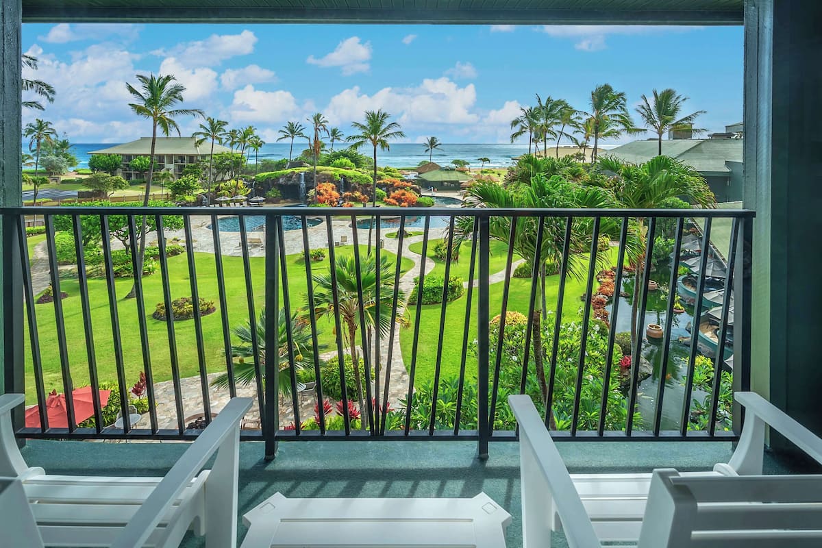 A balcony with a view of a landscaped garden, a pool, and the ocean.