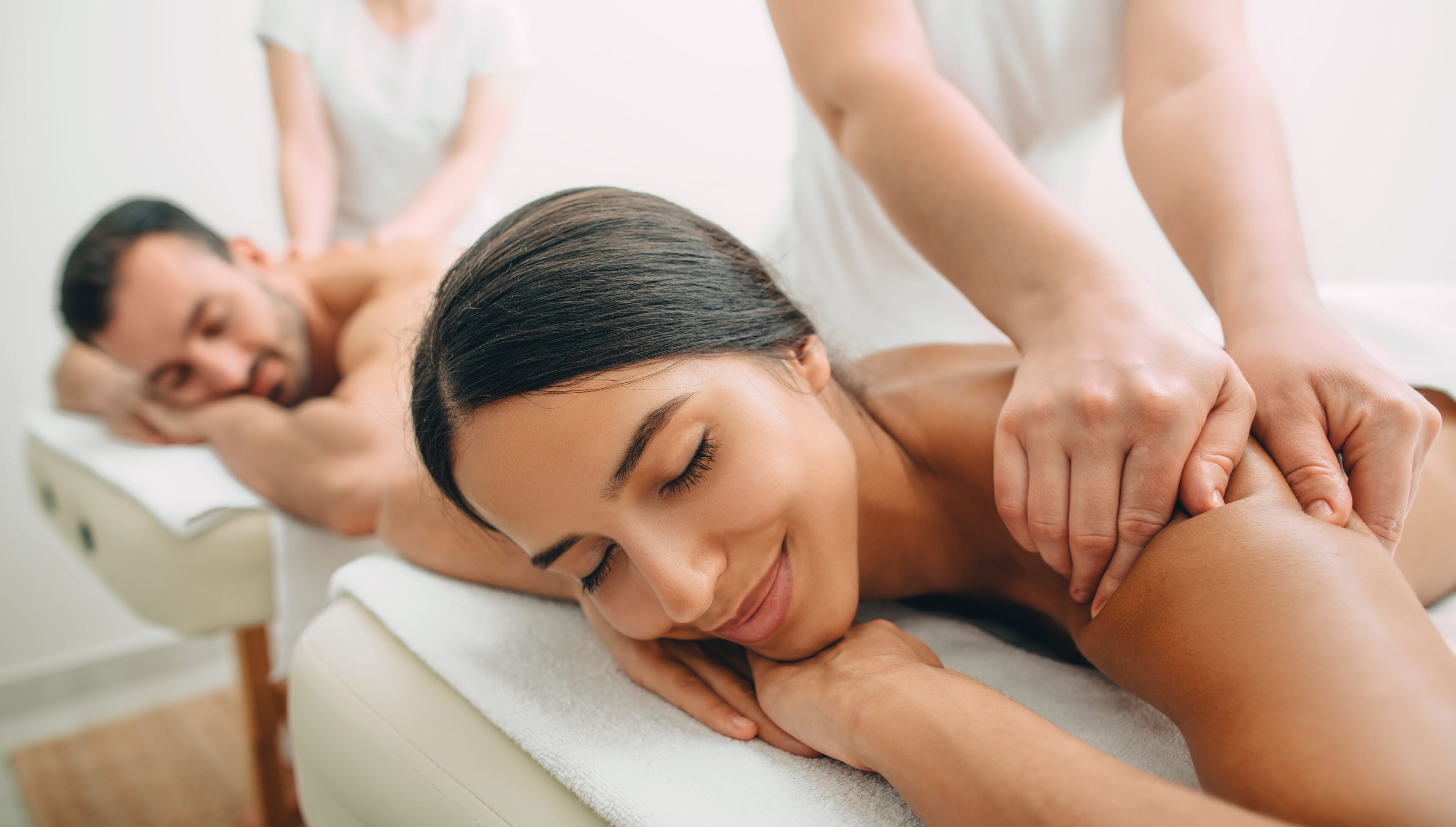 Une séance de massage thérapeutique dans un spa, où le client est allongé sur une table de massage, un thérapeute s’occupe de lui, et une autre personne se trouve à l’arrière-plan.