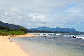 A beach with clear water, a sandy shore, and mountains in the background.