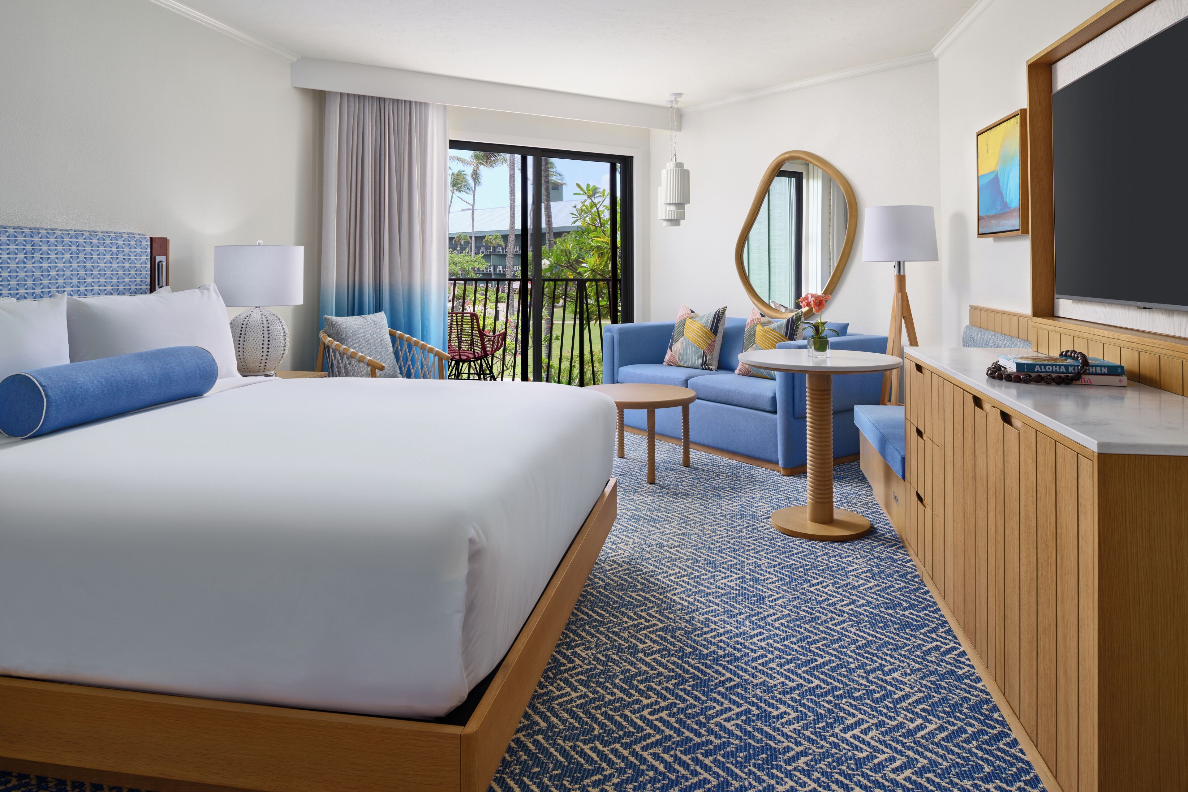 A hotel room with a large bed, a sofa, a small table, a mirror, and a TV.