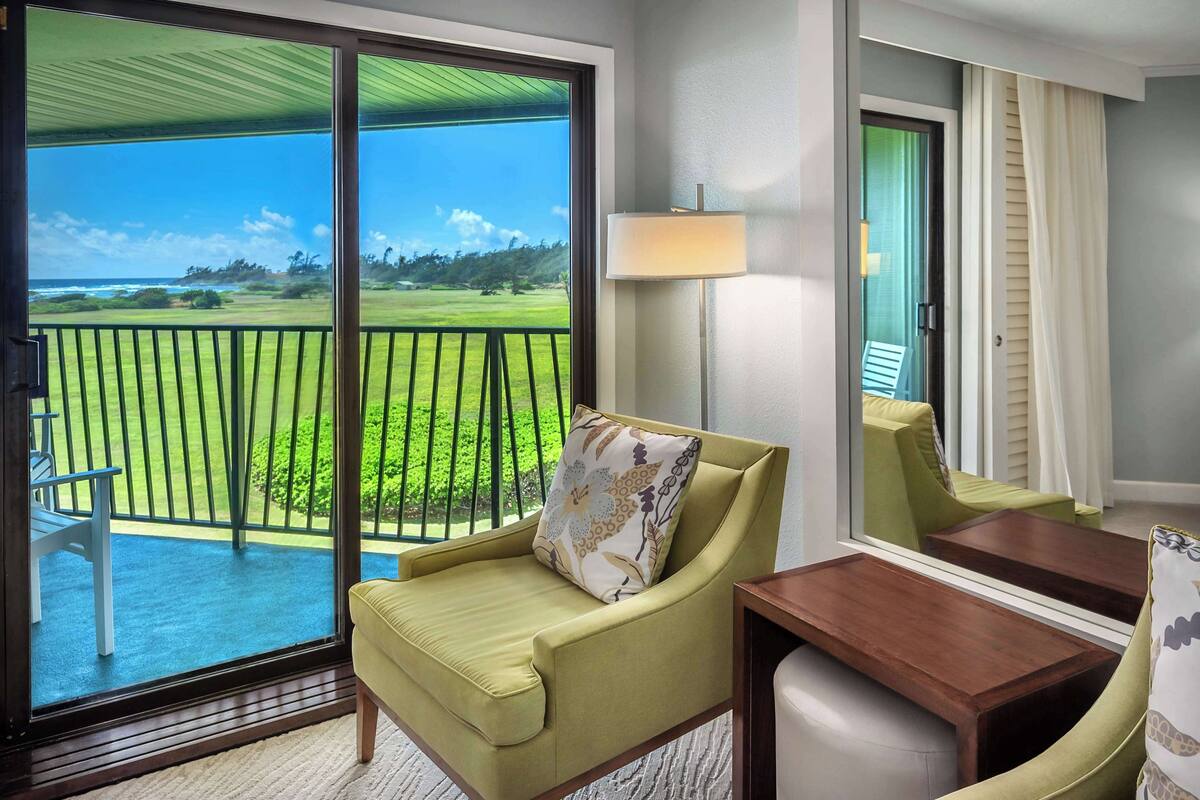 A room with a sliding glass door leading to a balcony with a view of a green landscape and ocean.