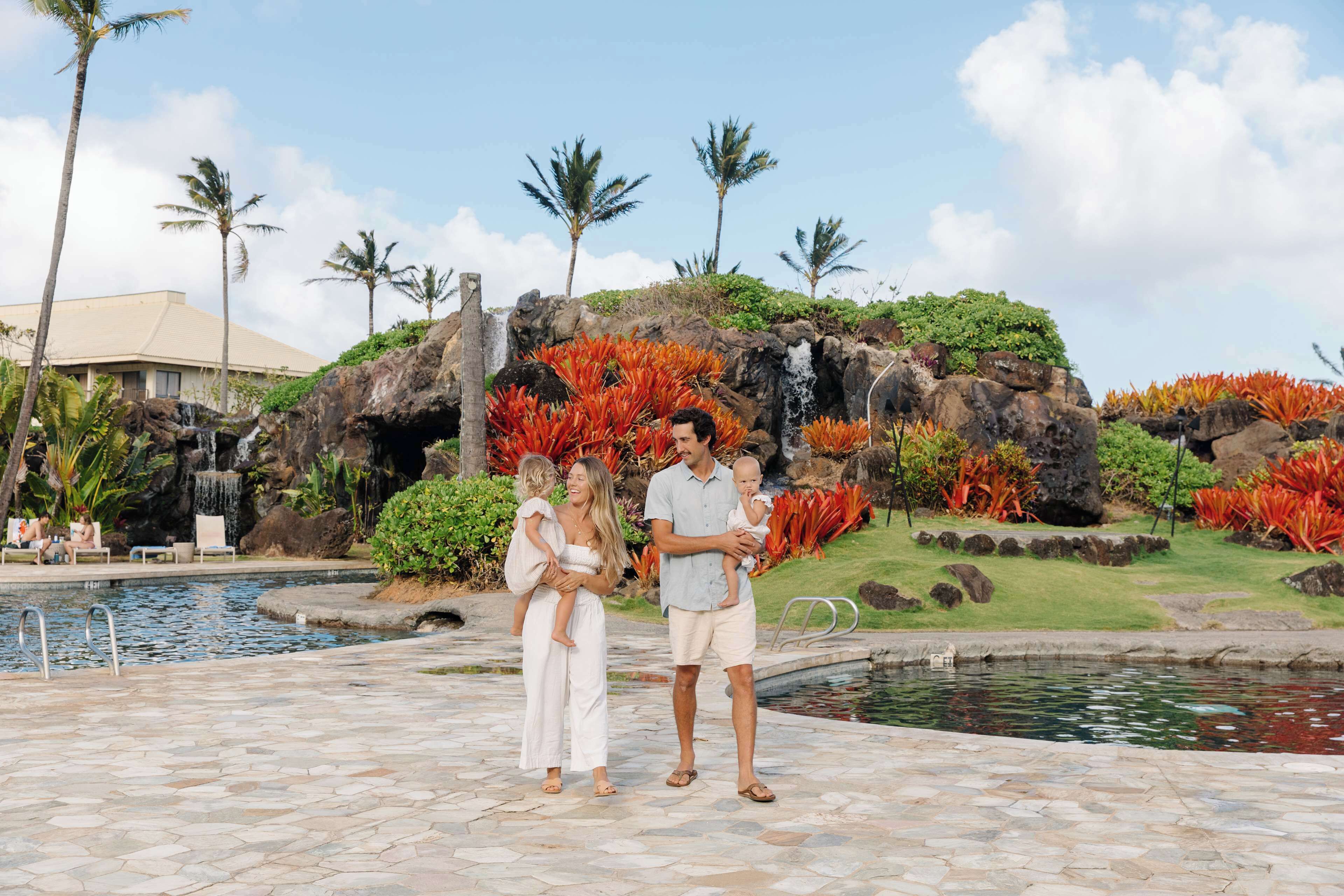A pool area with a waterfall, palm trees, and a building in the background.
