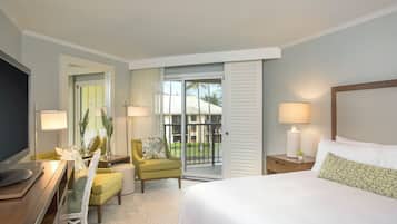 Habitación de hotel con una cama, un escritorio con computadora, una silla, una mesita de noche con lámpara y vistas al exterior.