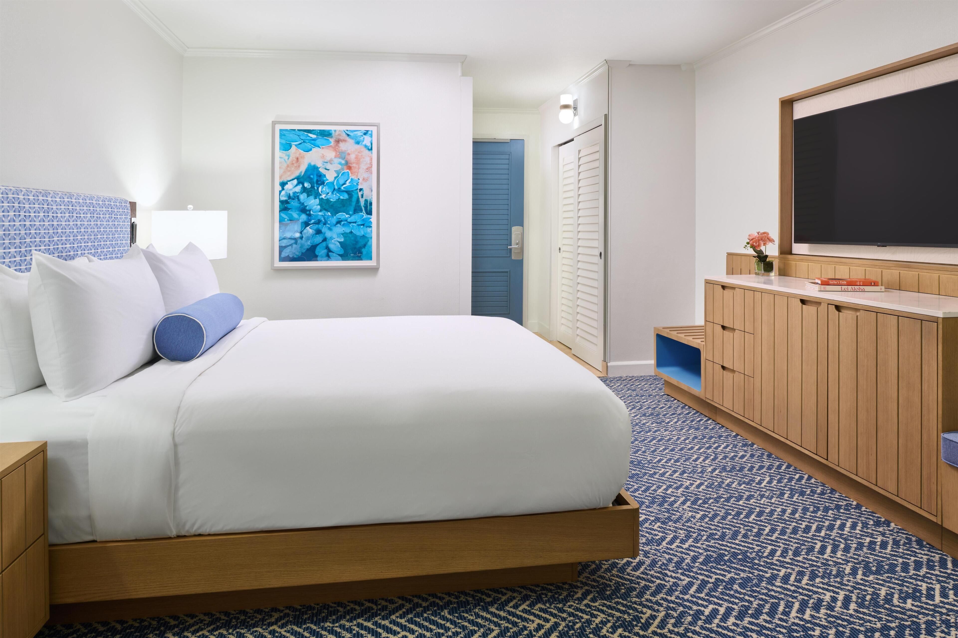 Een hotelkamer met een bed, een televisie, een schilderij en een kledingkast.