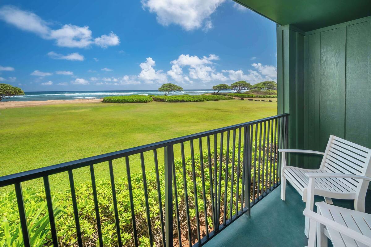 A balcony with a view of the ocean and a grassy area.