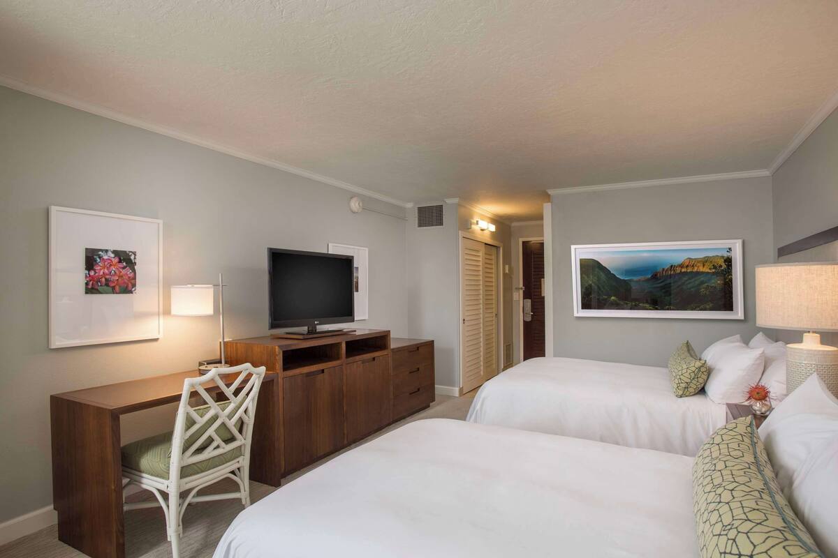 A hotel room with two beds, a desk with a TV, a chair, and artwork on the walls.