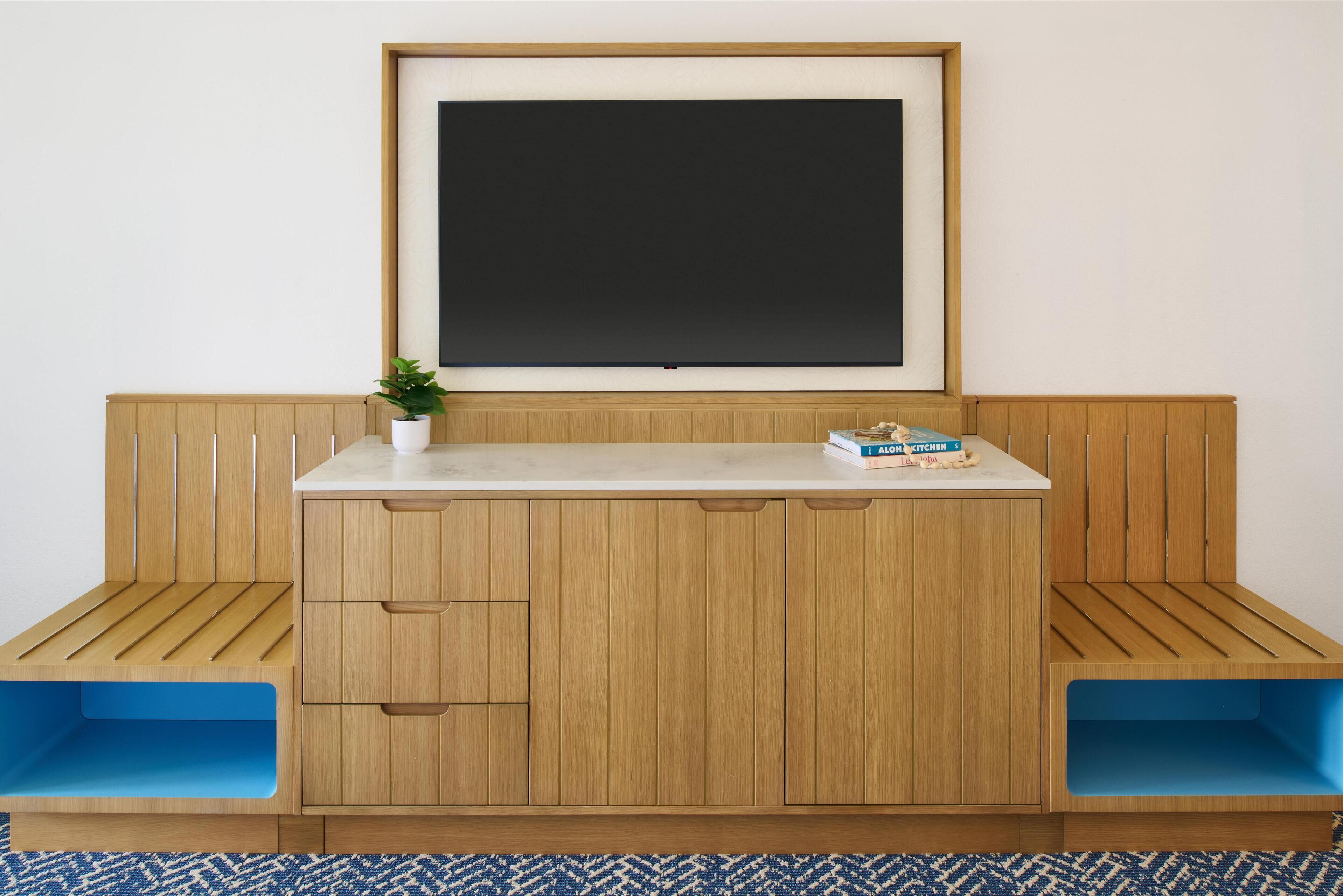 Une pièce comprenant un banc en bois servant de coin salon, un bureau blanc avec des tiroirs et un tableau noir encadré accroché au mur.
