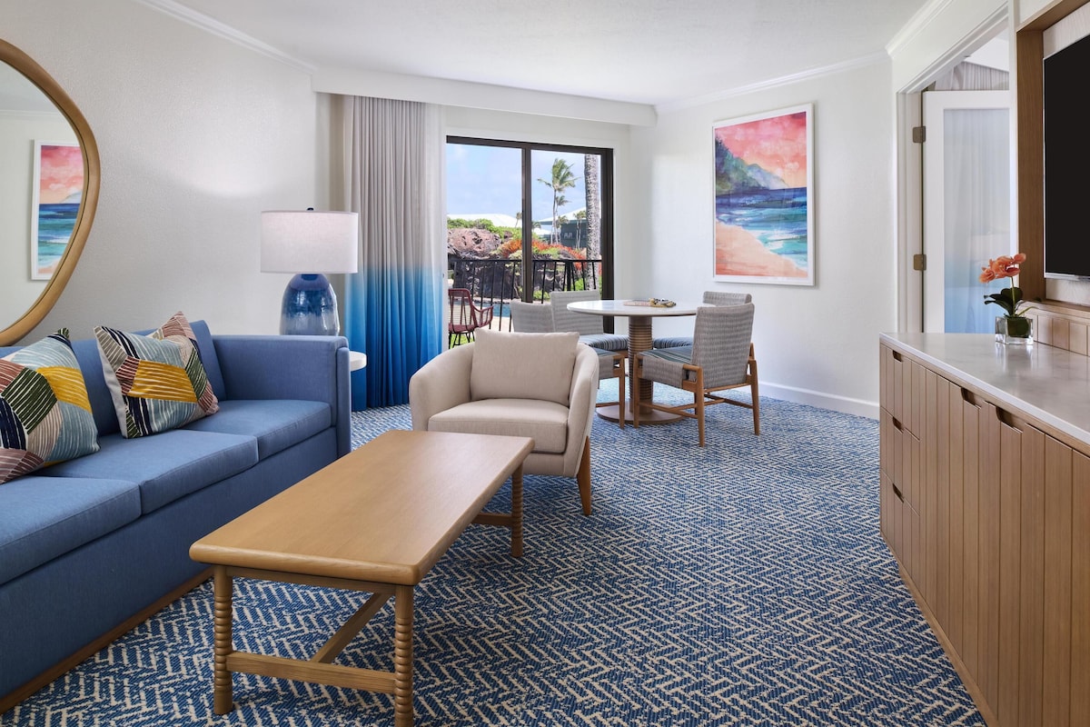Habitación de hotel con sofá, sillón, mesa y vista a la playa.