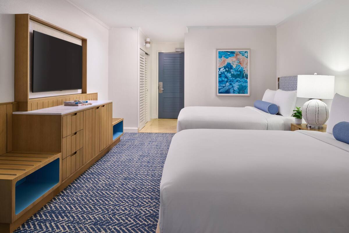 A hotel room with two beds, a TV, a painting, and a lamp.
