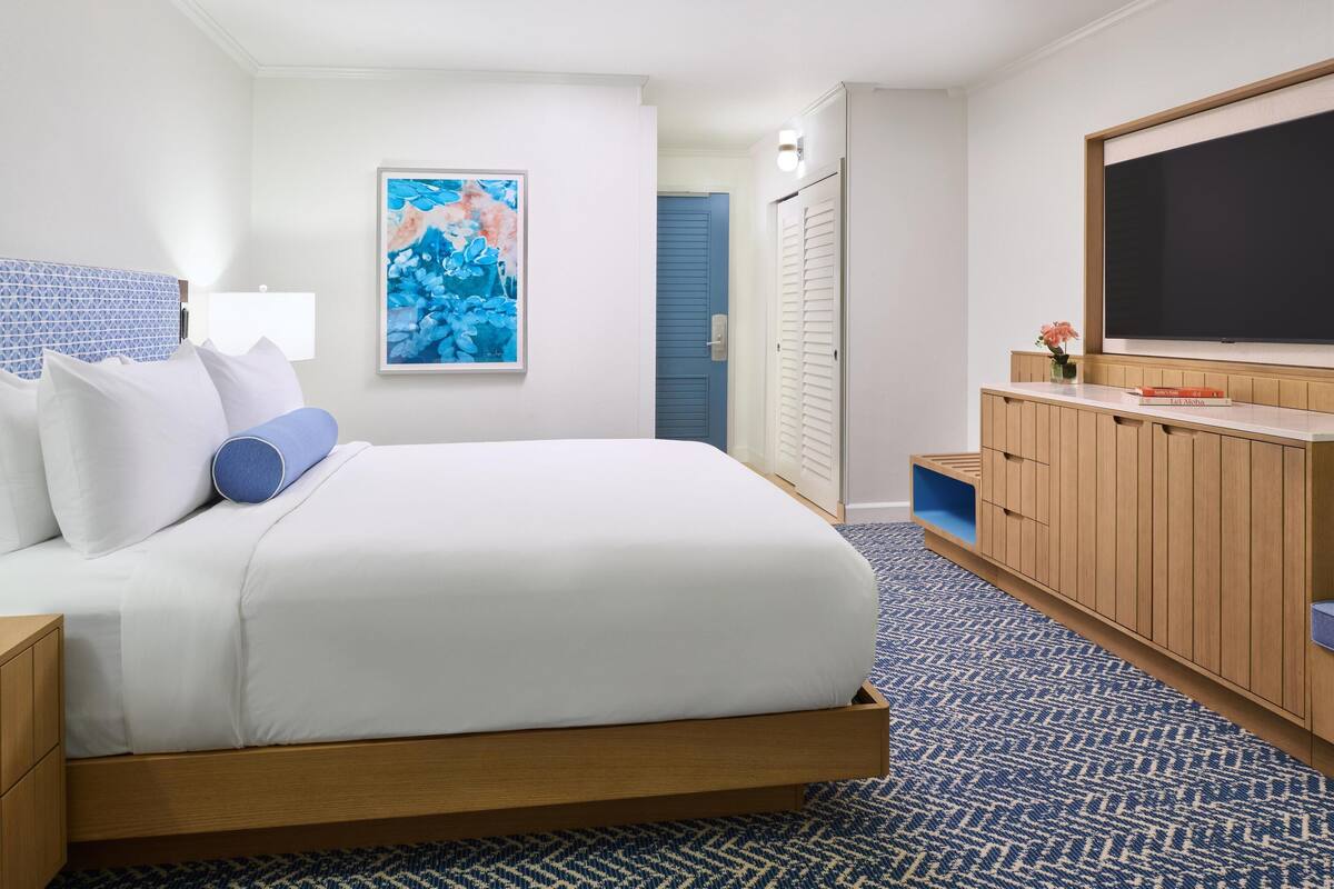 A hotel room with a bed, a TV, a painting, and a wardrobe.