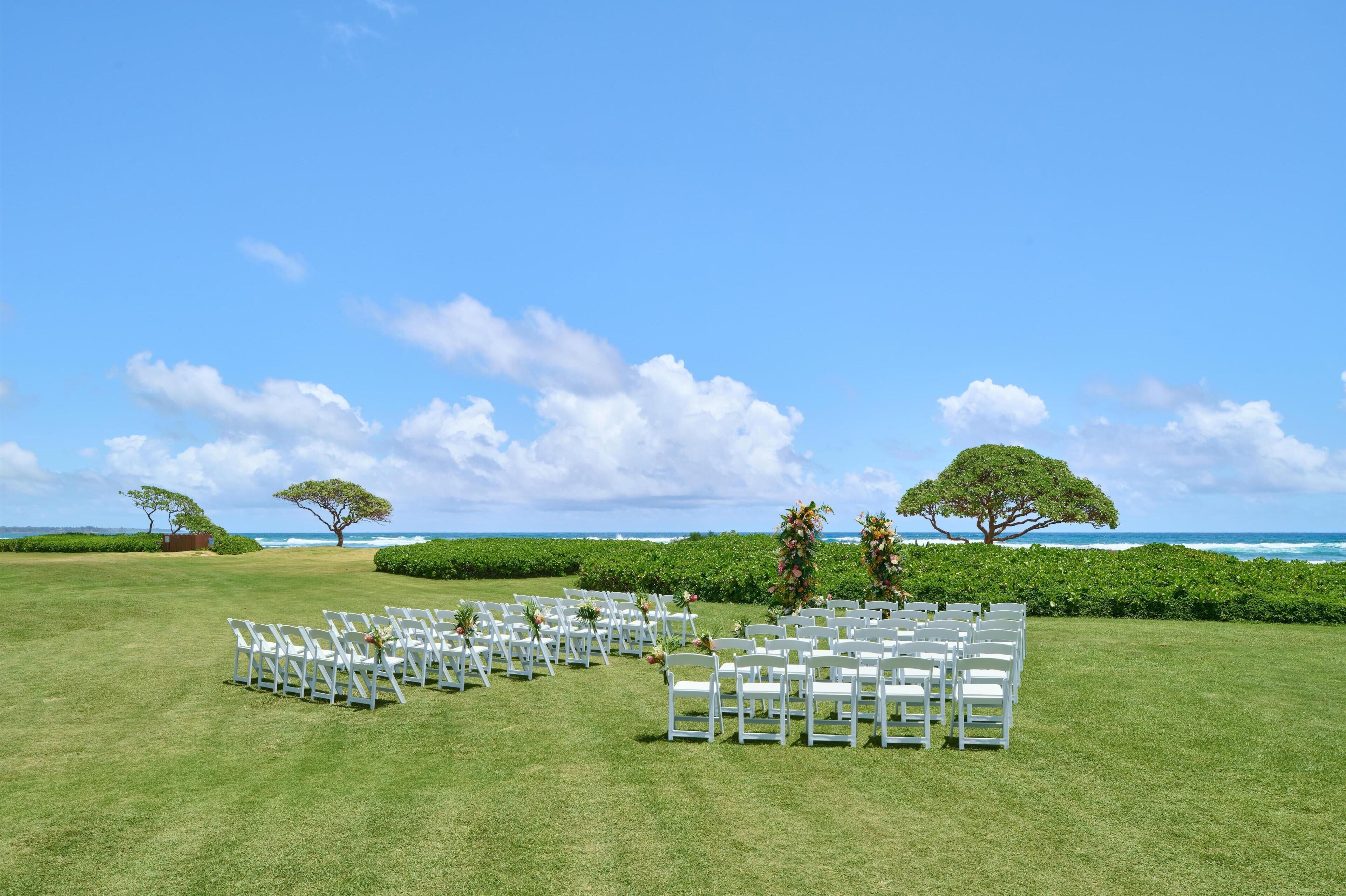 Un lieu de réception en plein air pour les mariages, avec des rangées de chaises blanches, une pelouse verdoyante et une vue sur l’océan.