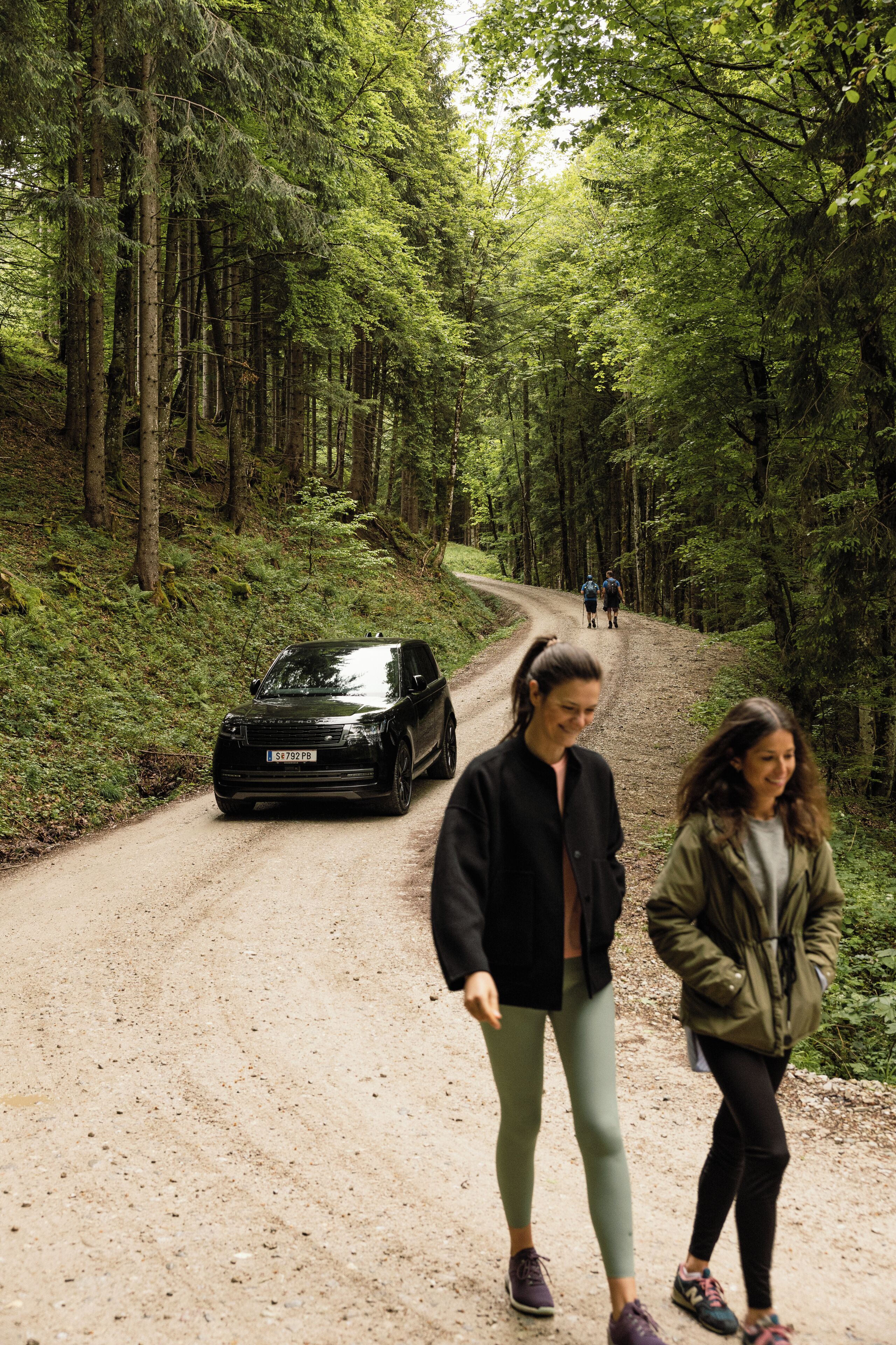 A forest road with a car and two people walking.