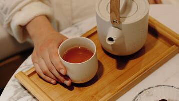 A wooden tray with a teapot and a cup of tea, a bowl of nuts and dried fruits, and a marble countertop.