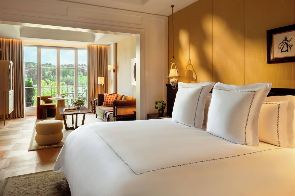A hotel room with a large bed, a balcony with curtains, a small table with a plant, and a sofa.