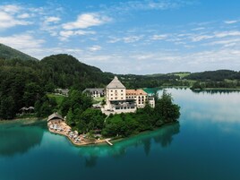 Um hotel à beira do lago, com um edifício grande rodeado por vegetação exuberante e um cais com área de estar ao ar livre.