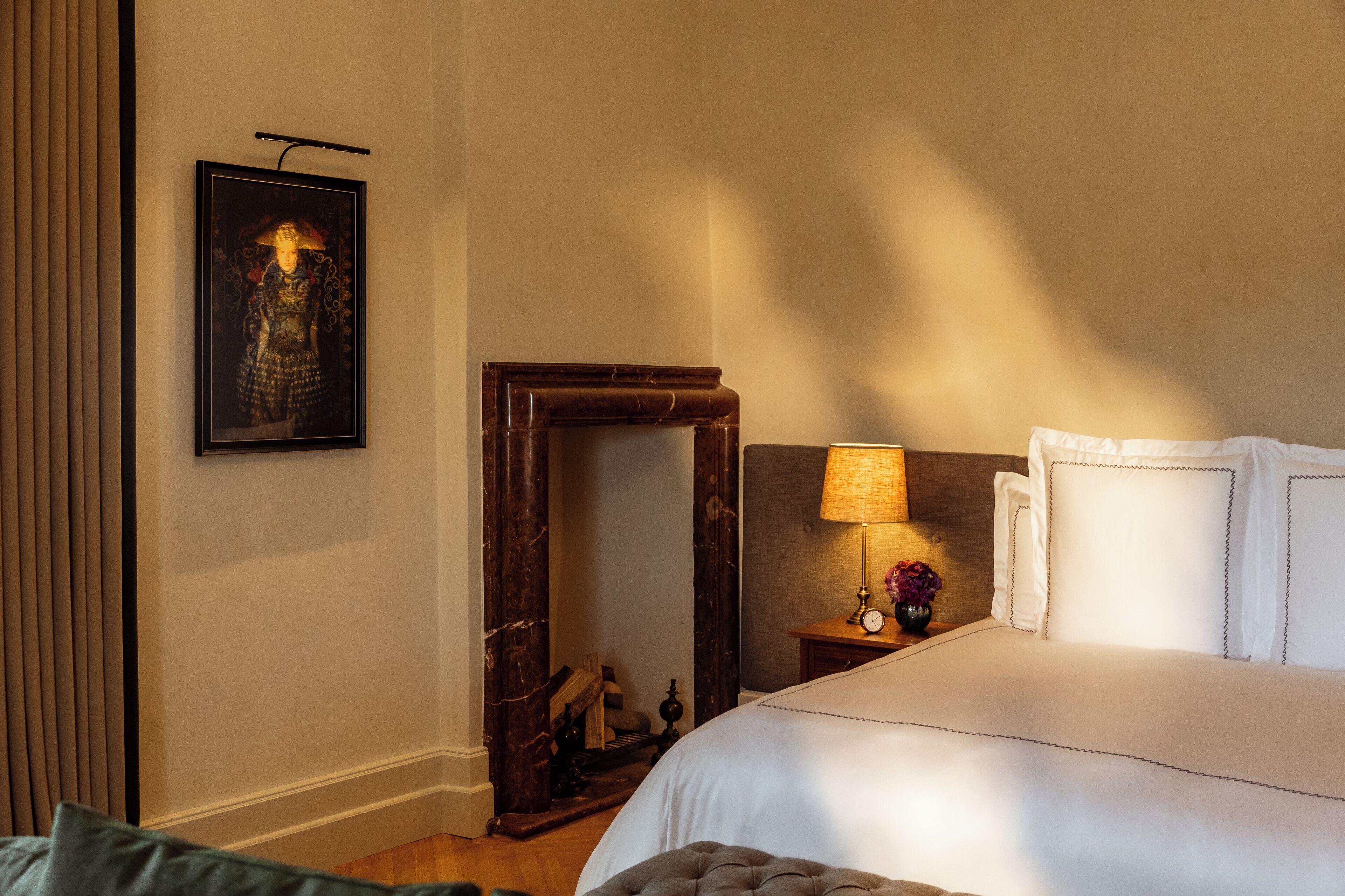A neatly arranged hotel room with a large bed, a bedside table with a lamp, a framed picture on the wall, and a mirror.