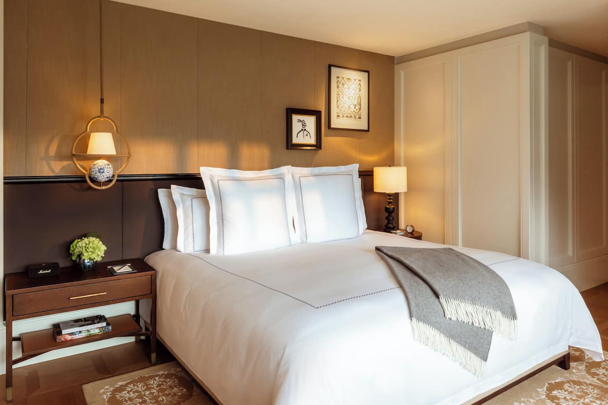 A neatly made bed with white linens, a bedside lamp, and a framed picture on the wall.