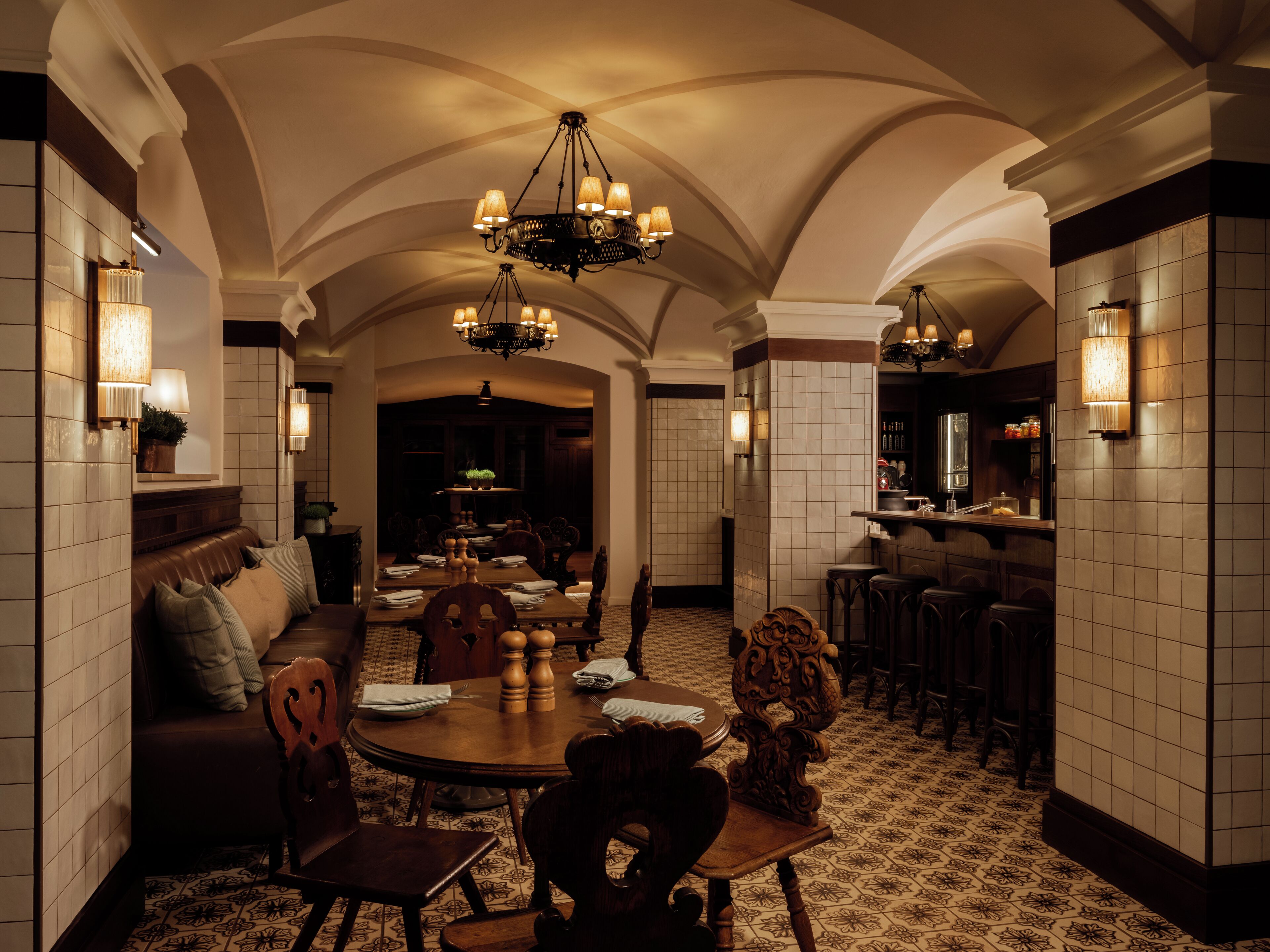 A spacious dining area with a high ceiling and ornate chandeliers, surrounded by a bar and seating areas.