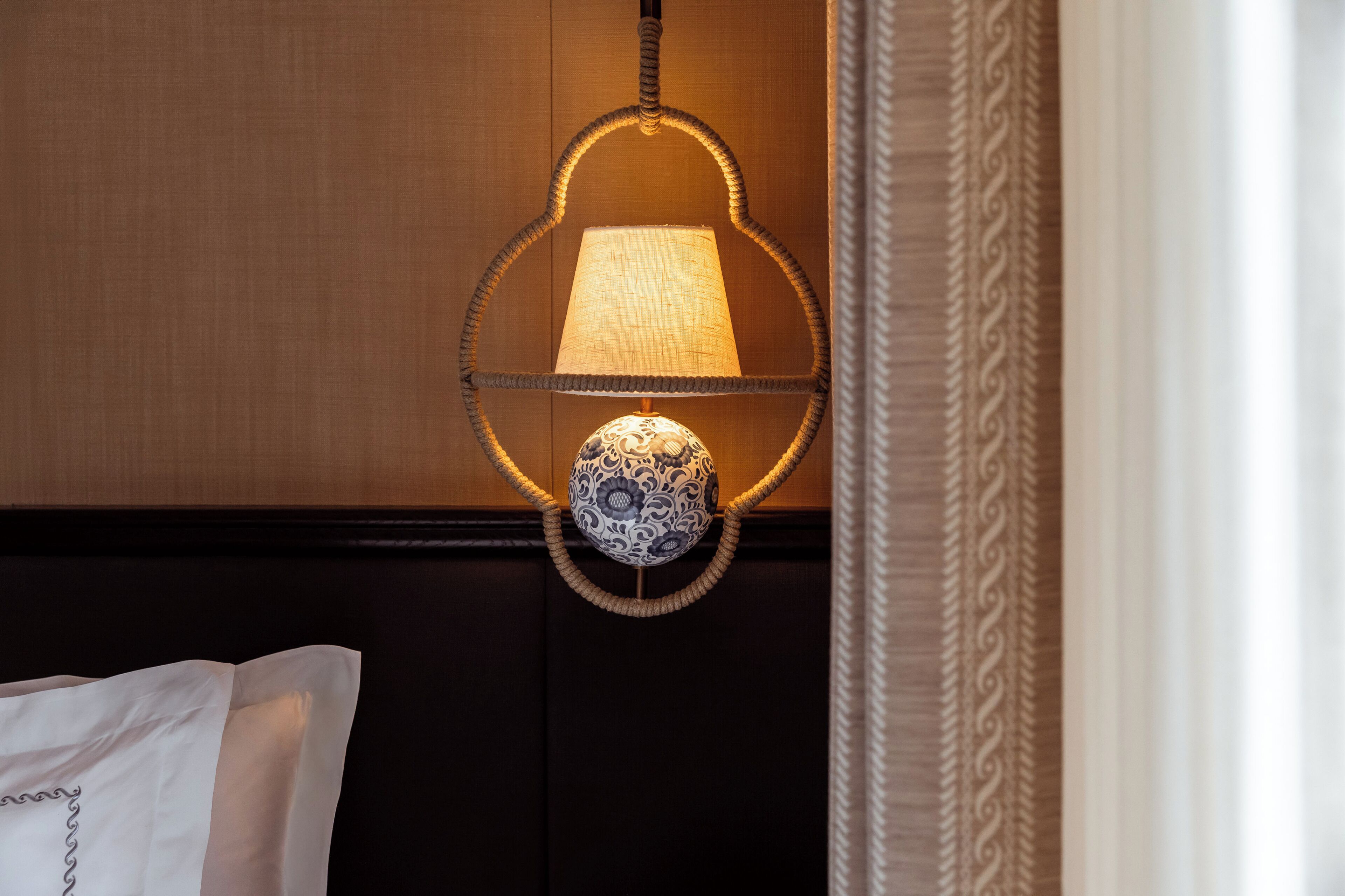 A wall-mounted lamp with a patterned shade and a decorative base, set against a wooden panel wall.