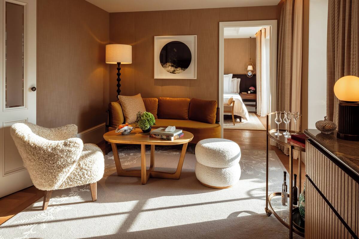 A cozy living room with a sofa, armchairs, a coffee table, and a lamp. There is a painting on the wall and a tray with glasses and books on the side table.