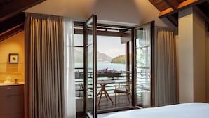 A bedroom with a large bed, wooden floor, and a view of a balcony with a table and chairs. - Rosewood Schloss Fuschl (Hof bei Salzburg)