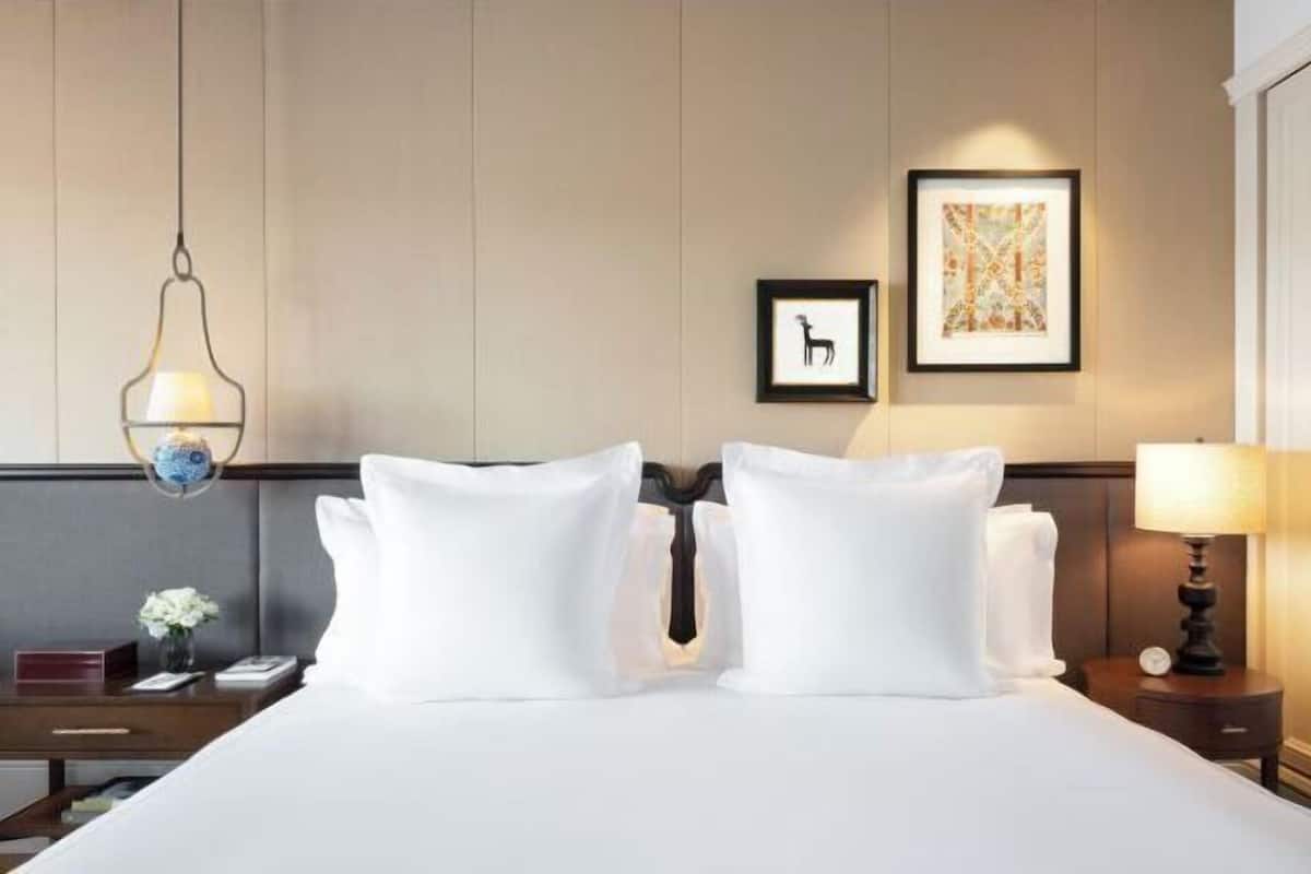 A hotel room with a bed, bedside tables, a hanging light fixture, framed artwork, and a wall-mounted clock.